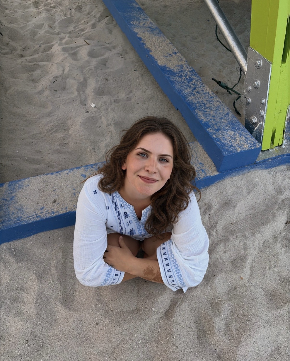 Dixie smiling on the beach in a white embroidered top